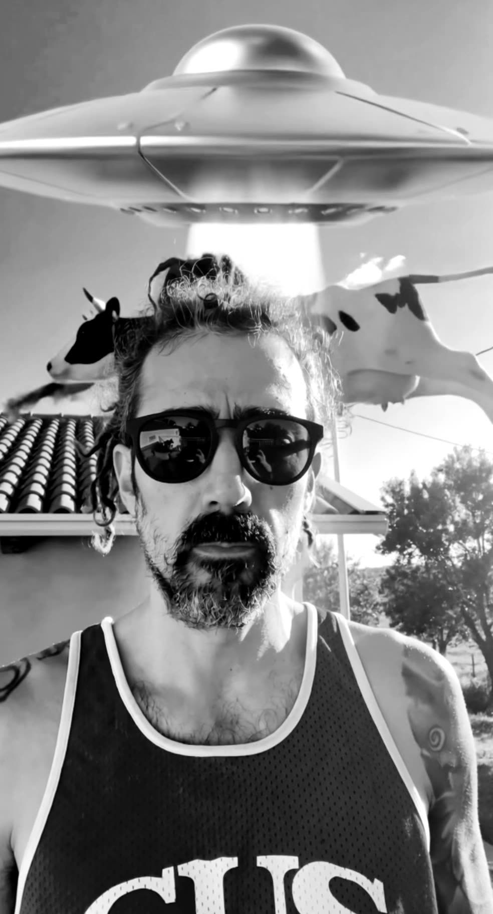 JANO portrait with sunglasses and tank top, a flying cow and a UFO behind him